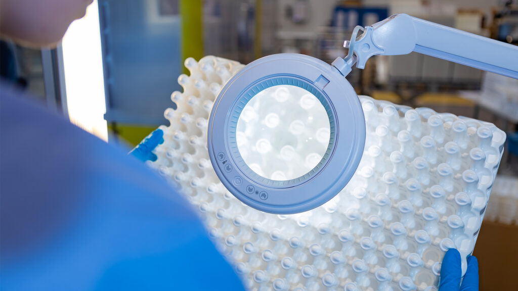 A person inspecting product quality under a magnifying lamp, focusing on fine details.